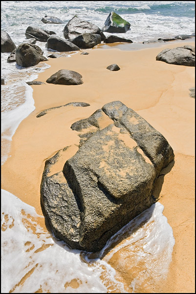 Rock partially covered with sand on a beach in Sanya, Hainan